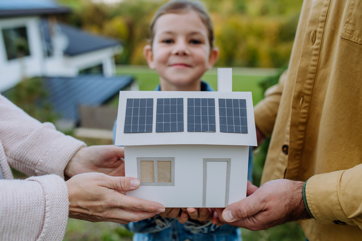 Close up of young family holding paper model of house with solar panels