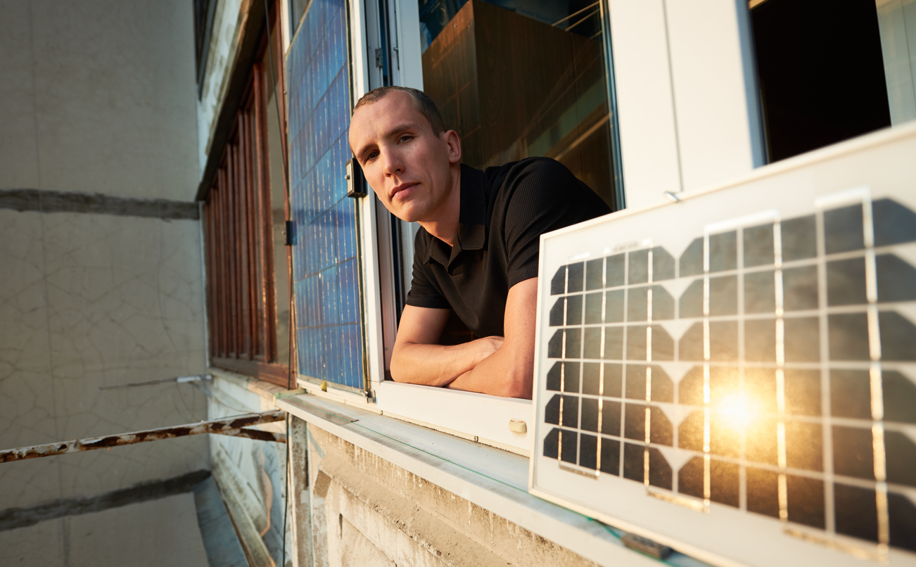 man on balcony of residential building with solar panel in which the sun is reflected